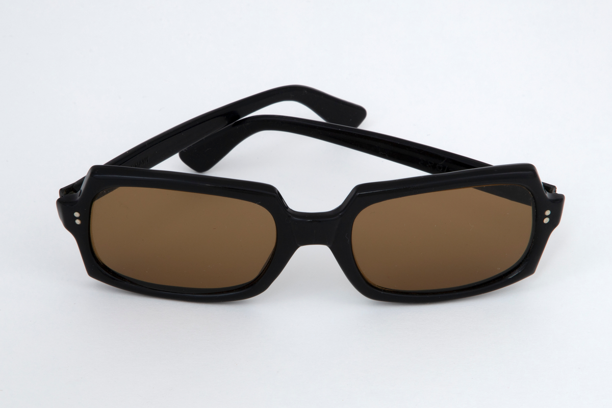 Solbriller med oval kantete plastglass og svart plastinnfatning med hengslede, svarte stenger.