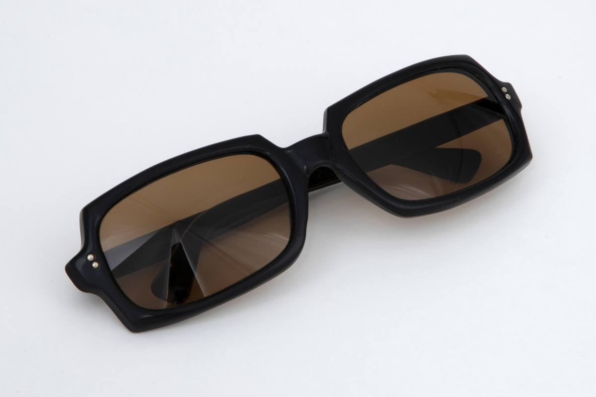 Solbriller med oval kantete plastglass og svart plastinnfatning med hengslede, svarte stenger.