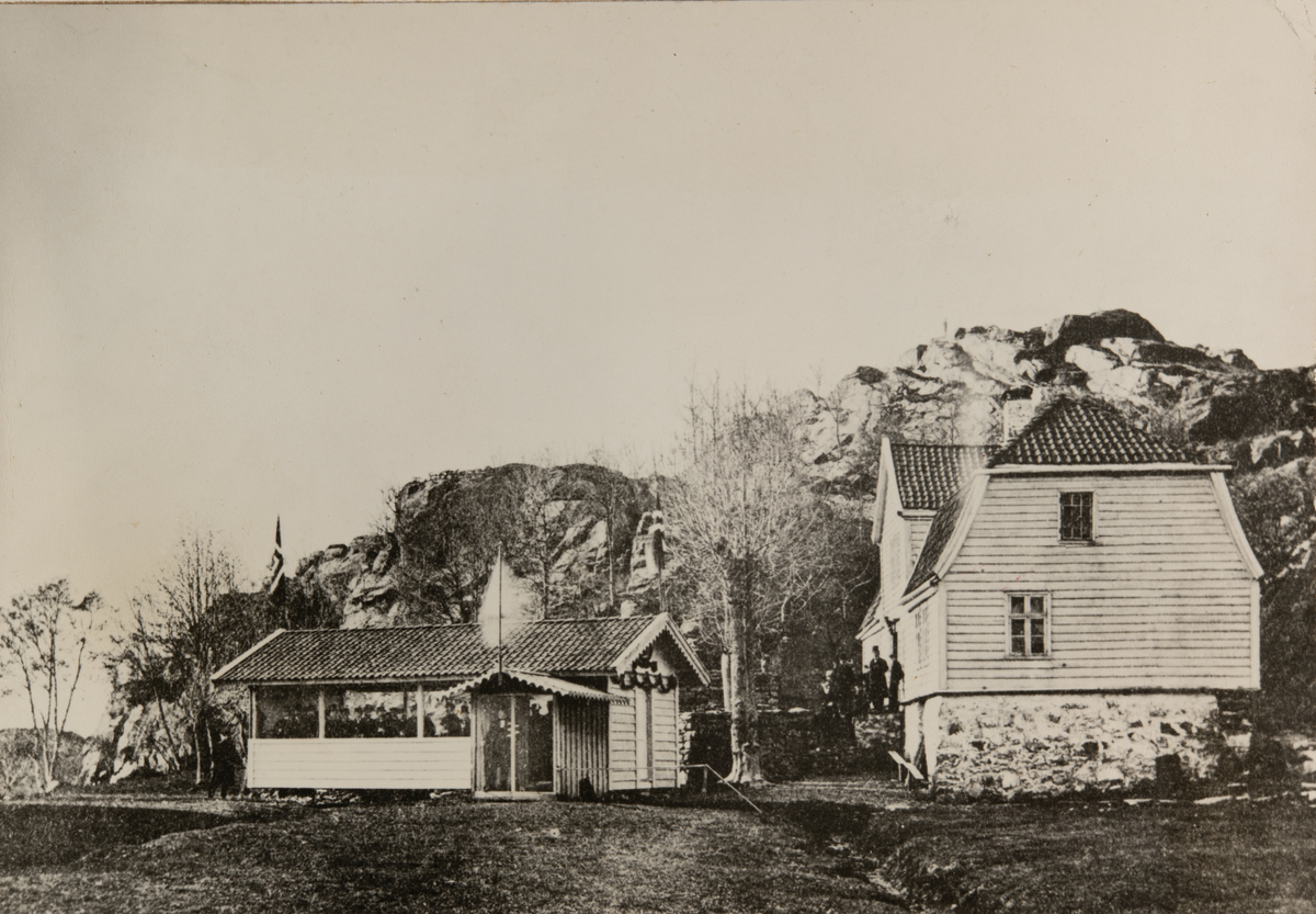 Et bolighus og et festpyntet uthus fullt av menn med flosshatt. Fjellknauser i bakgrunnen. Hovedhuset jægers Minde, senere Jægersminde 14, senere Breiviksvei 23.