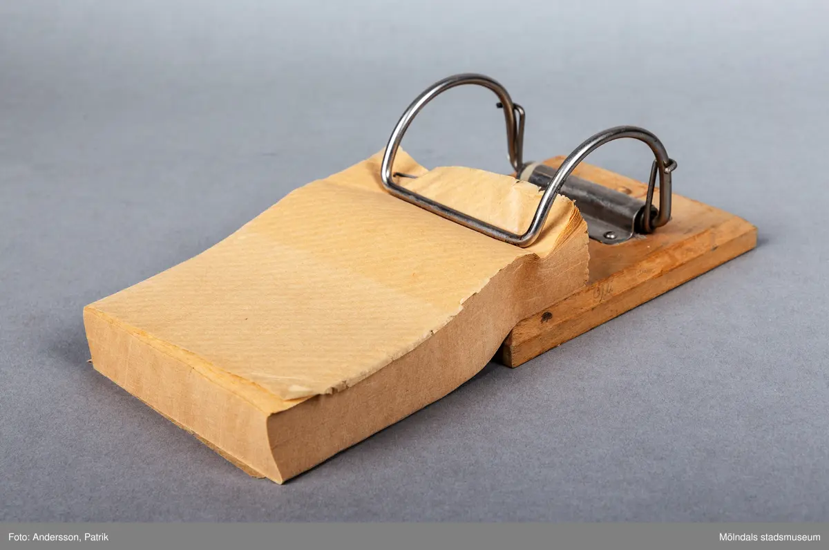 Toalettpappershållare med tillhörande papper. Pappret i hållaren är tillverkat av Papyrus i Mölndal.

Hållaren är en träplatta med en fastskruvad klämma av metall som håller toalettpappret. Pappersarken är ihophäftade i block.
En river loss ett ark eller flera och använder.