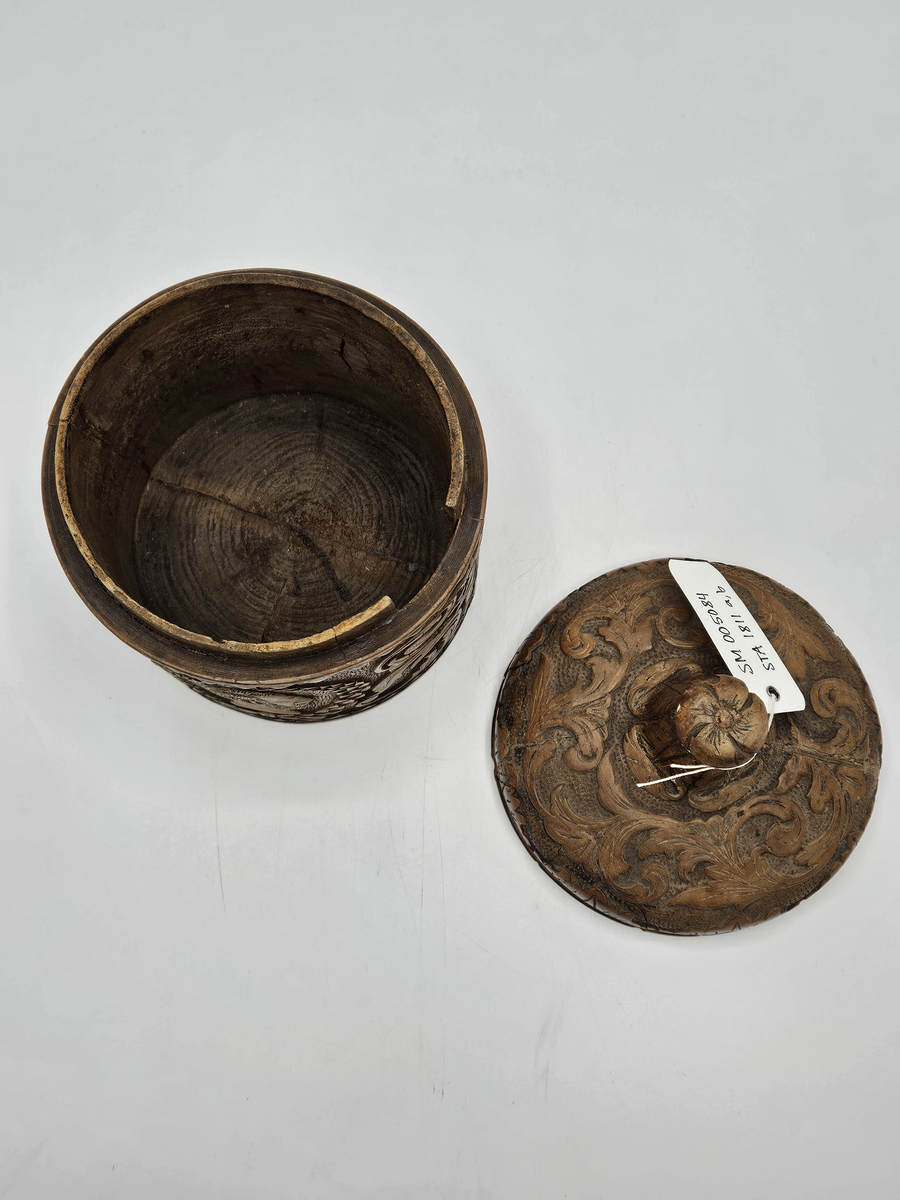 Tobaksburk av svarvad björk. Rund med skuren bladdekor, vapensköld, och porträtt av Karl XV inramad av en lagerkrans. Svagt välvt lock med hög knopp.  Material; Björk  Inköpt 1971 i antikaffär Gröna Terrinen(?) i Gamla Stan, för kr. 900 ;-