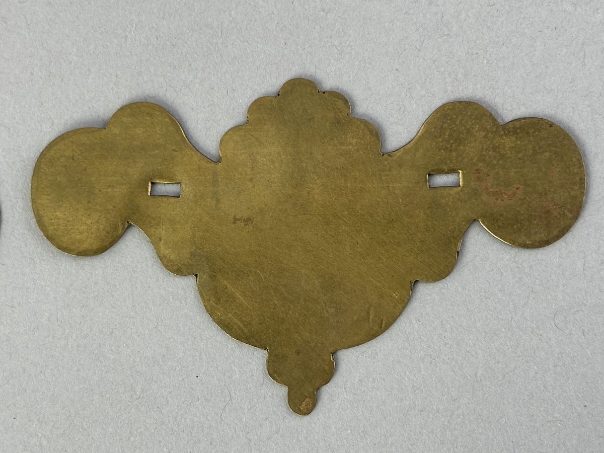 Handtagsbeslag av mässing. Modellerna saknar handtag. Modell a är dekorerad med punsat mönster.