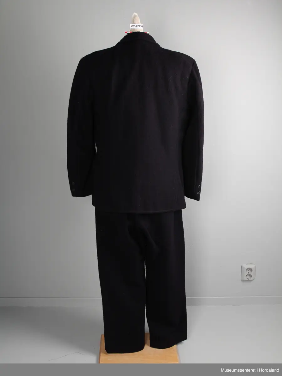 Herredress av vadmål beståande av bukse, jakke og dress:

1) Langbukse av mørkt blått vadmålstoff. Gylven er midt på framfor og har knappar og ei hekte. Buksa har ei lomme på kvar side. På baksida er det ein splitt i ryggen og eit spensel.

2) Jakke av mørkt blått vadmålstoff. Den har slag, opning framfor med fire knappar og knappehol, og dessutan to knappar nedst på ermane. Innvendig er jakka fôra med eit mørkt, rutete stoff. Jakka har to klafflommer med fôra klaffar i same rutete stoff.

3) Vest av mørkt blått vadmålstoff. Den har seks knappar med knappehol i opninga framfor, og dessutan to lommer på den eine sida og ei lomme på den andre sida. Bakstykket er av grått bomullsstoff med spennsel. Vesten er fôra.