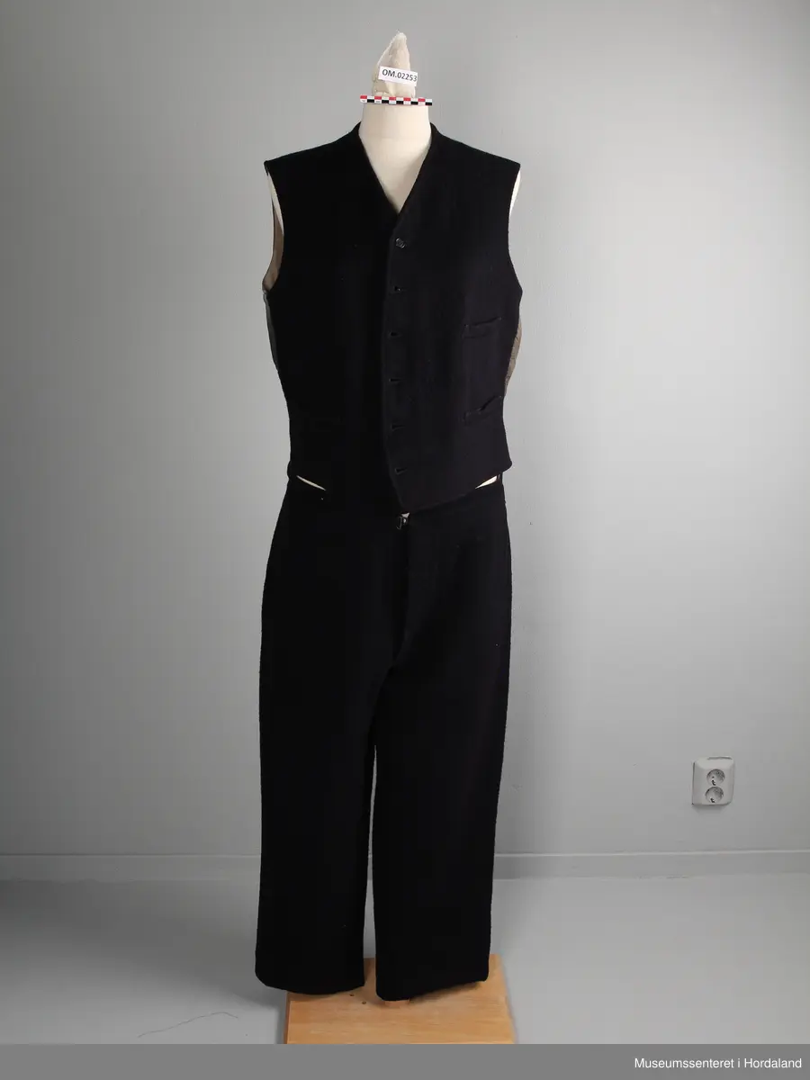 Herredress av vadmål beståande av bukse, jakke og dress:

1) Langbukse av mørkt blått vadmålstoff. Gylven er midt på framfor og har knappar og ei hekte. Buksa har ei lomme på kvar side. På baksida er det ein splitt i ryggen og eit spensel.

2) Jakke av mørkt blått vadmålstoff. Den har slag, opning framfor med fire knappar og knappehol, og dessutan to knappar nedst på ermane. Innvendig er jakka fôra med eit mørkt, rutete stoff. Jakka har to klafflommer med fôra klaffar i same rutete stoff.

3) Vest av mørkt blått vadmålstoff. Den har seks knappar med knappehol i opninga framfor, og dessutan to lommer på den eine sida og ei lomme på den andre sida. Bakstykket er av grått bomullsstoff med spennsel. Vesten er fôra.