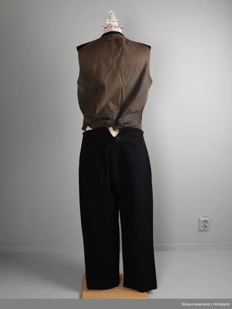 Herredress av vadmål beståande av bukse, jakke og dress:

1) Langbukse av mørkt blått vadmålstoff. Gylven er midt på framfor og har knappar og ei hekte. Buksa har ei lomme på kvar side. På baksida er det ein splitt i ryggen og eit spensel.

2) Jakke av mørkt blått vadmålstoff. Den har slag, opning framfor med fire knappar og knappehol, og dessutan to knappar nedst på ermane. Innvendig er jakka fôra med eit mørkt, rutete stoff. Jakka har to klafflommer med fôra klaffar i same rutete stoff.

3) Vest av mørkt blått vadmålstoff. Den har seks knappar med knappehol i opninga framfor, og dessutan to lommer på den eine sida og ei lomme på den andre sida. Bakstykket er av grått bomullsstoff med spennsel. Vesten er fôra.