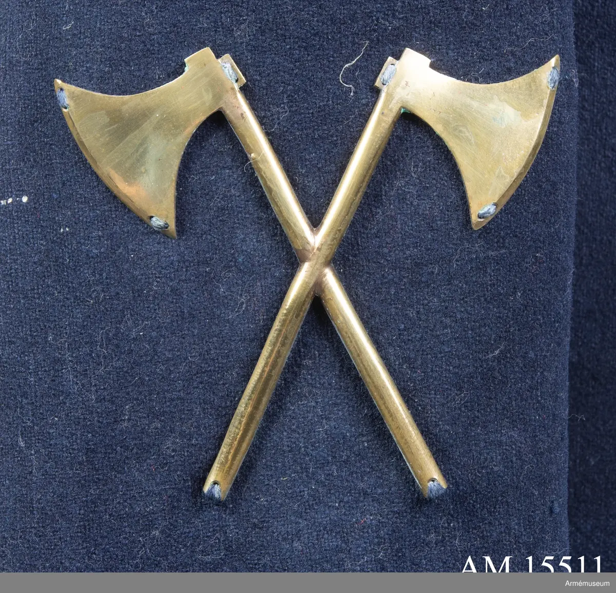 Två distinktionstecken av mässing i form av två korslagda yxor. Tecknen har 8 hål för fastsättning på uniformen.
Tecknen är fastsydda på fracken AM.015502:s ärmar.

Till distinktionstecknen hör en modelletikett med rött vaxsigill och följande text:
"Modell till Öfver-Timmermans distinction, att fästas på båda Jack ärmarne, Nådigast approberad under dena dag, Stockholms Slott d. 26 Aprill 1832, På nådigaste befallning M. Brahe, General Adjutant för Armén".
Sigillet pryds av Lilla Riksvapnet i mitten med följande text runt om: "Konungens Gen. Adjuts. Exprd. för Arméen".