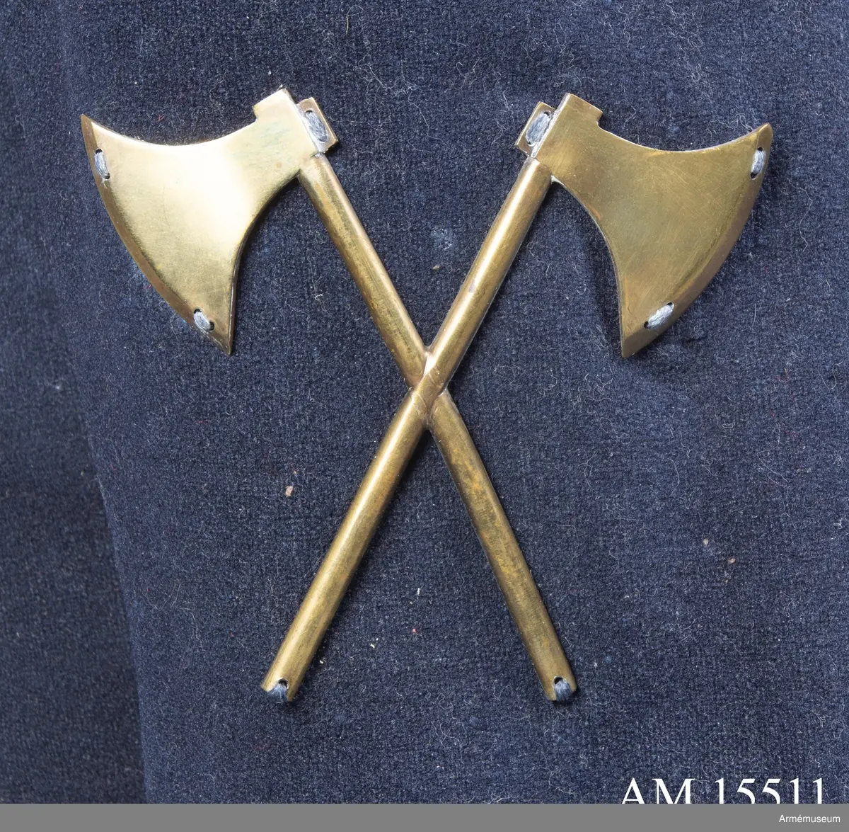 Två distinktionstecken av mässing i form av två korslagda yxor. Tecknen har 8 hål för fastsättning på uniformen.
Tecknen är fastsydda på fracken AM.015502:s ärmar.

Till distinktionstecknen hör en modelletikett med rött vaxsigill och följande text:
"Modell till Öfver-Timmermans distinction, att fästas på båda Jack ärmarne, Nådigast approberad under dena dag, Stockholms Slott d. 26 Aprill 1832, På nådigaste befallning M. Brahe, General Adjutant för Armén".
Sigillet pryds av Lilla Riksvapnet i mitten med följande text runt om: "Konungens Gen. Adjuts. Exprd. för Arméen".