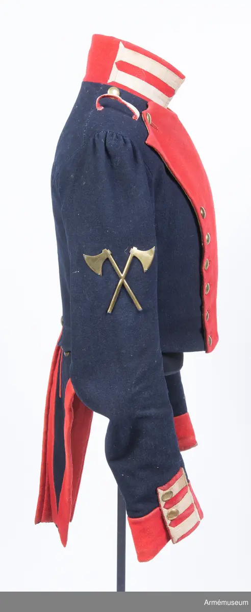 Två distinktionstecken av mässing i form av två korslagda yxor. Tecknen har 8 hål för fastsättning på uniformen.
Tecknen är fastsydda på fracken AM.015502:s ärmar.

Till distinktionstecknen hör en modelletikett med rött vaxsigill och följande text:
"Modell till Öfver-Timmermans distinction, att fästas på båda Jack ärmarne, Nådigast approberad under dena dag, Stockholms Slott d. 26 Aprill 1832, På nådigaste befallning M. Brahe, General Adjutant för Armén".
Sigillet pryds av Lilla Riksvapnet i mitten med följande text runt om: "Konungens Gen. Adjuts. Exprd. för Arméen".