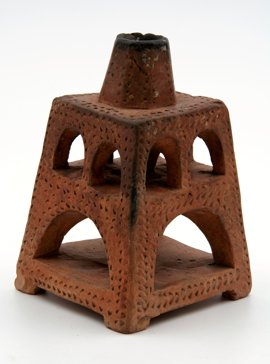 Ljusstake av bränt lergods. Fyrkantig, med öppningar med rundbågar. Ljushållare för ett ljus.