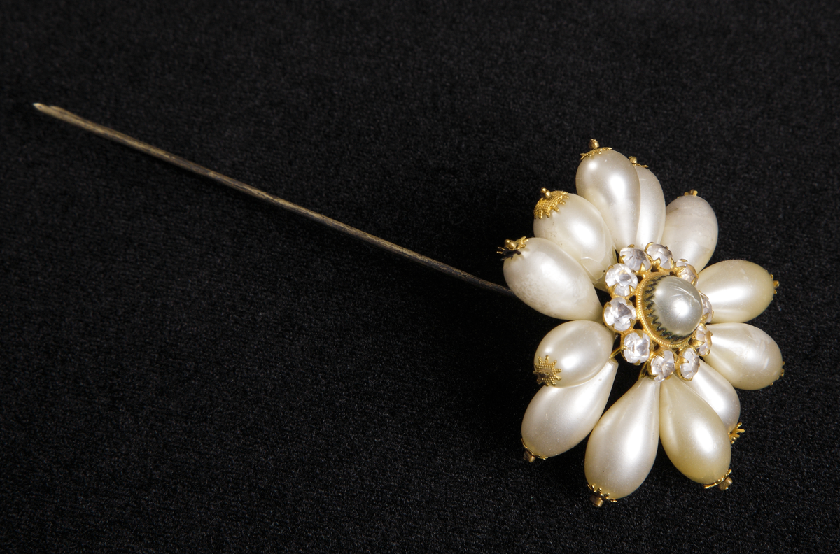 6 st hårnålar burna av Christina Nilsson i operan Lohengrin. Själva nålhuvudet, format som en blomma i imiterade pärlor.