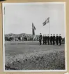 Löjtnant Per Lindblom för svenska örlogsflaggan förbi kungliga läktaren. I bakgrunden syns folkmängden som har samlats för att följer ceremonin.