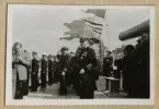 Bilden visar en amiral och sjöofficerare som har tagit uppställning ombord på pansarskeppet Sverige under besöket av kung Gustav V. I bakgrunden syns ett flertal fotografer som dokumenterar händelsen.