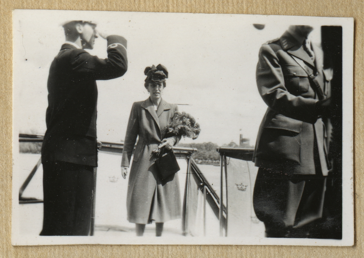 Kronprinsessan Louise kliver ombord på pansarskepp Sverige. I famnen bär hon ett blombukett och en väska. En sjöofficerare utför en militärisk hälsning.