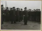 Bilden visar besättningen på ett pansarskepp. I mitten syns en amiral som talar till manskapet som har tagit uppställning på höger sidan. Bakom amiralen står dem högre befälen.