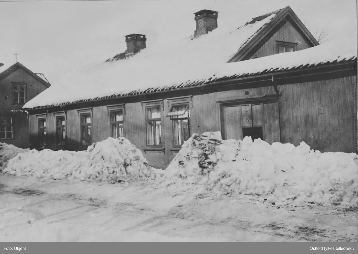 Carsten Andresens hus i St. Marie gate, Sarpsborg (revet). Høye snøkanter foran huset. Andresen var lærer og byens første kirkesanger.
Datering ukjent. Hans hus lå i St. Marie gate , skrått overfor Methodistkirken, litt lenger ned. Solgt etter fru Anne Marie Andersens død i 1900, visstnok til Emanuel (ell. Immanuel?) Pettersen (ell. Petterson), og revet.  På forsidenortert med fargeblyant på kartong: "Gammeldagse senefald gjorde også sin nytte."
KAn være rundt St. Marie gate 75 (?).