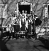 Avslutning vid Grimslövs folkhögskola.
Ett antal unga kvinnor och män poserar utanför ett trähus, iförda
Värendsdräkt.