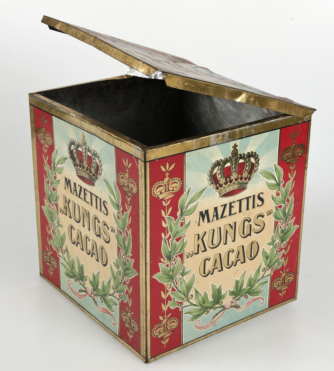 Målad i rött, guld, grönt och blått. Text "Mazettis Kungs cacao".
