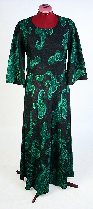 Långklänning, svart botten med persiskt tryckt mönster i olika gröna nyanser. Rund vid halsringning. Vid trekvartslång isydd tvåsömsärm. Delad under bysten med en 10 cm bred och slätt påsydd linning. Baktill en 59 cm lång dragkedja. Kjolen har 7 st utställda våder.