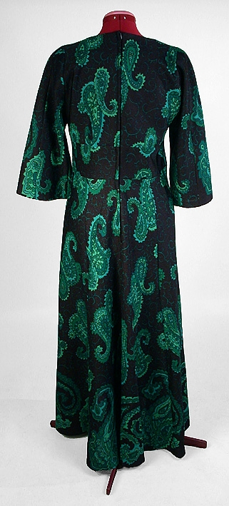 Långklänning, svart botten med persiskt tryckt mönster i olika gröna nyanser. Rund vid halsringning. Vid trekvartslång isydd tvåsömsärm. Delad under bysten med en 10 cm bred och slätt påsydd linning. Baktill en 59 cm lång dragkedja. Kjolen har 7 st utställda våder.