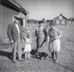 Alfhild Ericsson t.h. står med en hundvalp, en man, en kvinna och ett barn. Flera hus i bakgrunden, 1929.