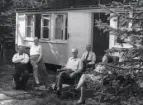 Folke Bäcklund sittandes med sällskap vid Bildstensharen, i bakgrunden en stuga och skog, 1930-tal.