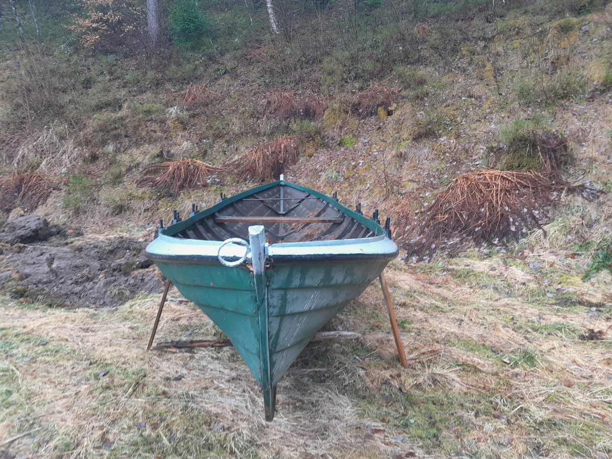 Båt. Klinkbygd trebåt med 5 omfar. Otring. Grønmåla øvst, svart nedst utvendig. Kvitmåla øvste omfar/kant. Fire par keipar.  Keipane er plassert oppå den kvitmåla kanten, inntil øvste kant.