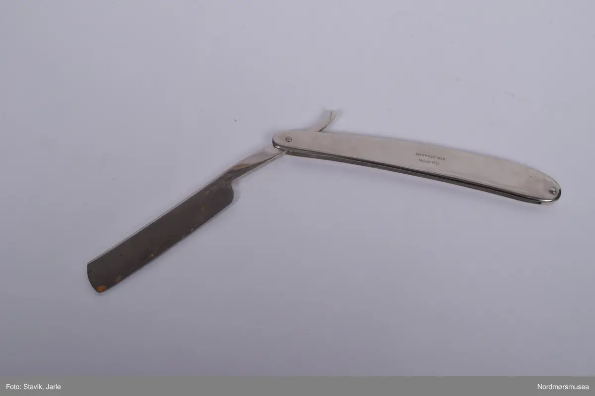 Barberkniv i rustfritt stål, sammenleggbar. Til \å fjerne hår før medisinske inngrep. Bladet vippes ut v.h.a hendel på enden.