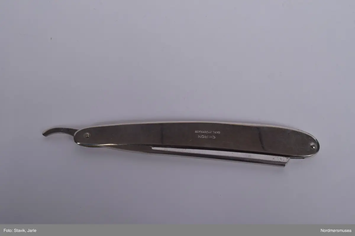 Barberkniv i rustfritt stål, sammenleggbar. Til \å fjerne hår før medisinske inngrep. Bladet vippes ut v.h.a hendel på enden.