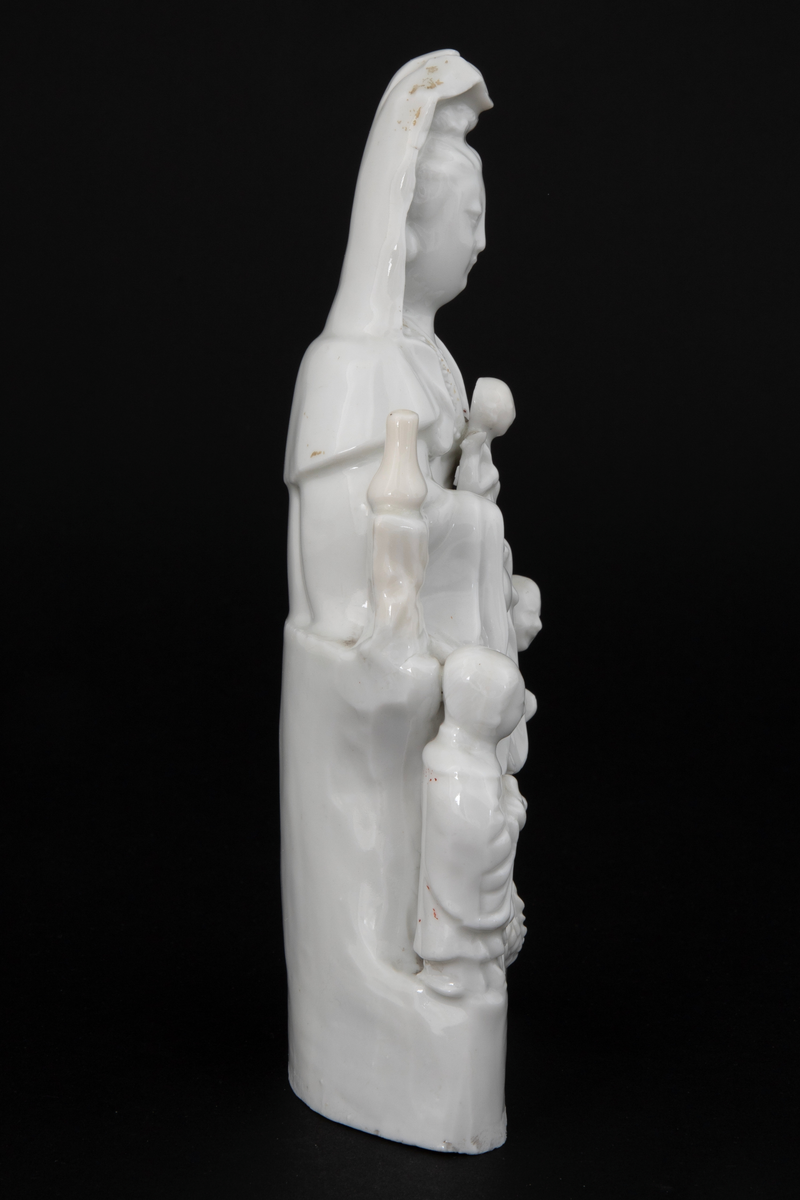 Figuren representerer den buddhistiske bodhisattavaen Guanyin, en barmhjertighetsgudinne. Hun er avbildet sittende med et barn i fanget. Barnet holder et ruyisepter. Guanyin er flankert av to figurer. Dette er hennes to akolytter, dragekongens datter Longnu, jadejomfuren, og Shoukai, det gylne barn. Disse to er i utgangspunktet taostiske figurer, og var assistentene til de åtte udødelige. Avbildet på denne måten er hun kjent som den "høyaktede hvitkledde." Ved basen under Guanyins føtter finner vi en drage. Guanyins posisjonering over en drage refererer til hennes stauts som Putuofjellets beskyttende bodhisattava og sørhavenes herskerinne og fiskernes beskytter.