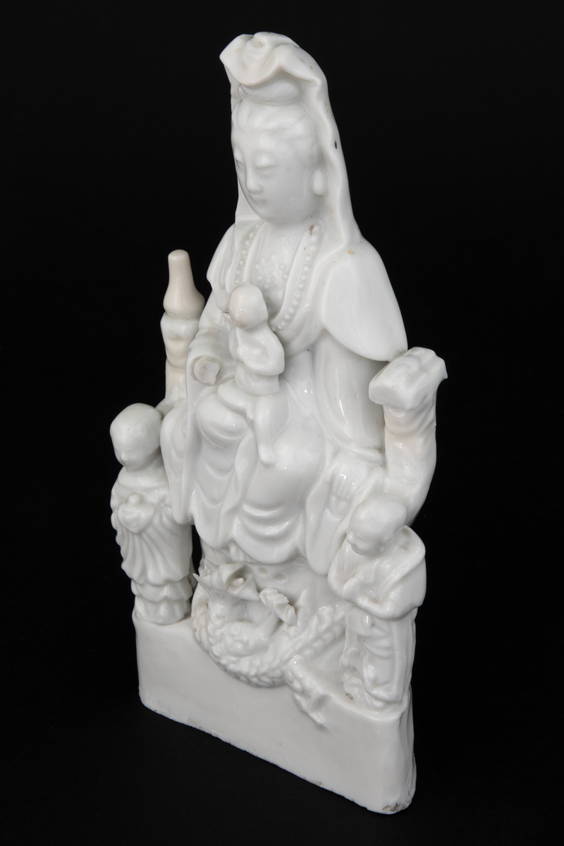 Figuren representerer den buddhistiske bodhisattavaen Guanyin, en barmhjertighetsgudinne. Hun er avbildet sittende med et barn i fanget. Barnet holder et ruyisepter. Guanyin er flankert av to figurer. Dette er hennes to akolytter, dragekongens datter Longnu, jadejomfuren, og Shoukai, det gylne barn. Disse to er i utgangspunktet taostiske figurer, og var assistentene til de åtte udødelige. Avbildet på denne måten er hun kjent som den "høyaktede hvitkledde." Ved basen under Guanyins føtter finner vi en drage. Guanyins posisjonering over en drage refererer til hennes stauts som Putuofjellets beskyttende bodhisattava og sørhavenes herskerinne og fiskernes beskytter.