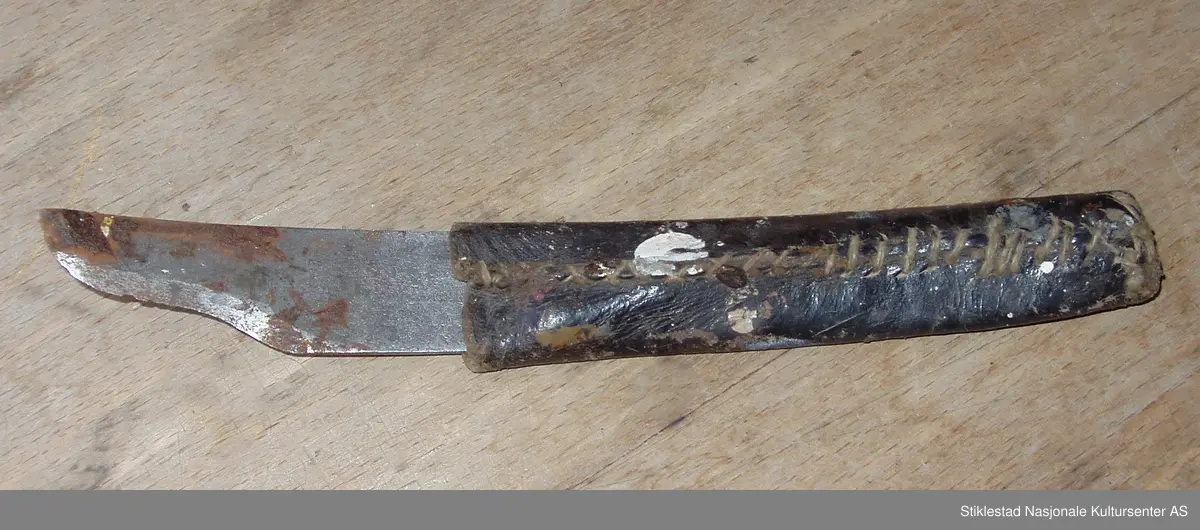 Krum skomakerkniv med påsydd skinnhylse. Rust på knivblad, hvit maling på skinnhylse.