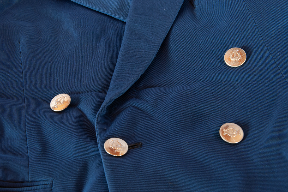 Uniformsjakke. Blå gabardin, foret med blå kunstsilke, Ermene foret med hvit/grå kunstsilke. Gullig pyntebånd på ermer og epoljetter.
Blanke knapper med symbol på epoljetter og i dobbelknepping. Tre utvendige lommer, pluss en innvendig.