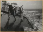 Två sjömän försöker att hålla sig på benen ombord på flygplanskryssaren Gotland som rullar starkt under en storm i Nordsjön. Ändå verka båda två ha det mycket rolig. Mannen till höger har en frälsarkrans runt halsen.