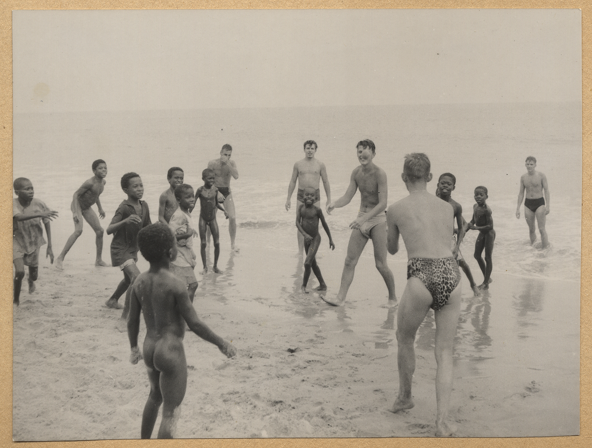 Svenska sjömän från flygplanskryssaren Gotland lekar med svarta barn på en strand i Afrika.