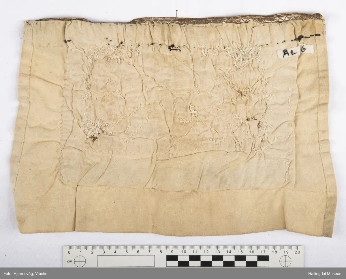 Håndsydd brystduk i lin, ull og silke med fløyelsband og glassperler i blomstermønster. Ubleika linlerret på baksida.
