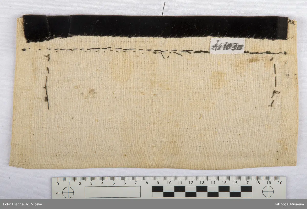 Kvit bomullslerret på baksida og bretta noko over på framsida. På frramsida raud vadmål med påsydd geometrisk mønster av små, runde glasperler. Øvst på brystduken ein svart fløyelskant.