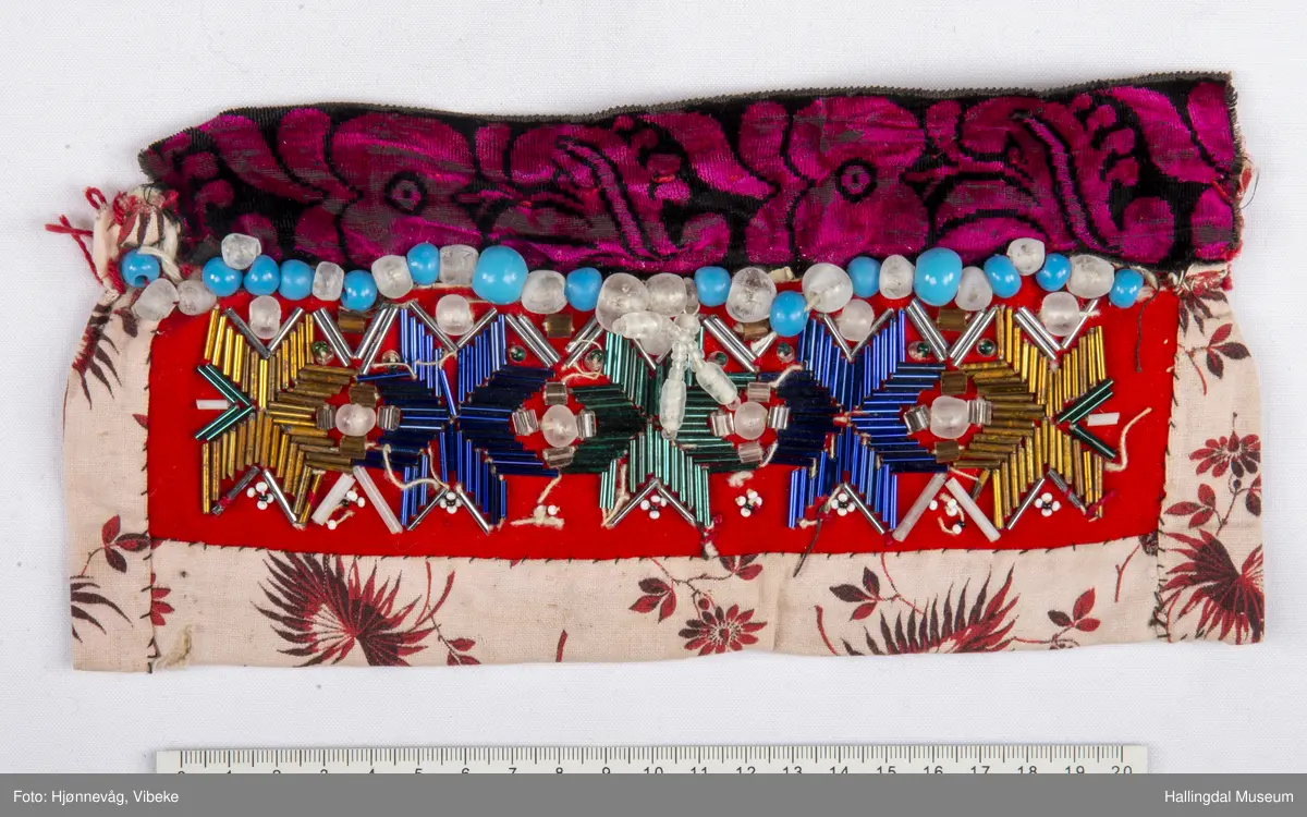 5 åttebladroser av lange glasperler, små perler rundt, over desse ei rad med store, kuleforma, blanke og lys blå perler.