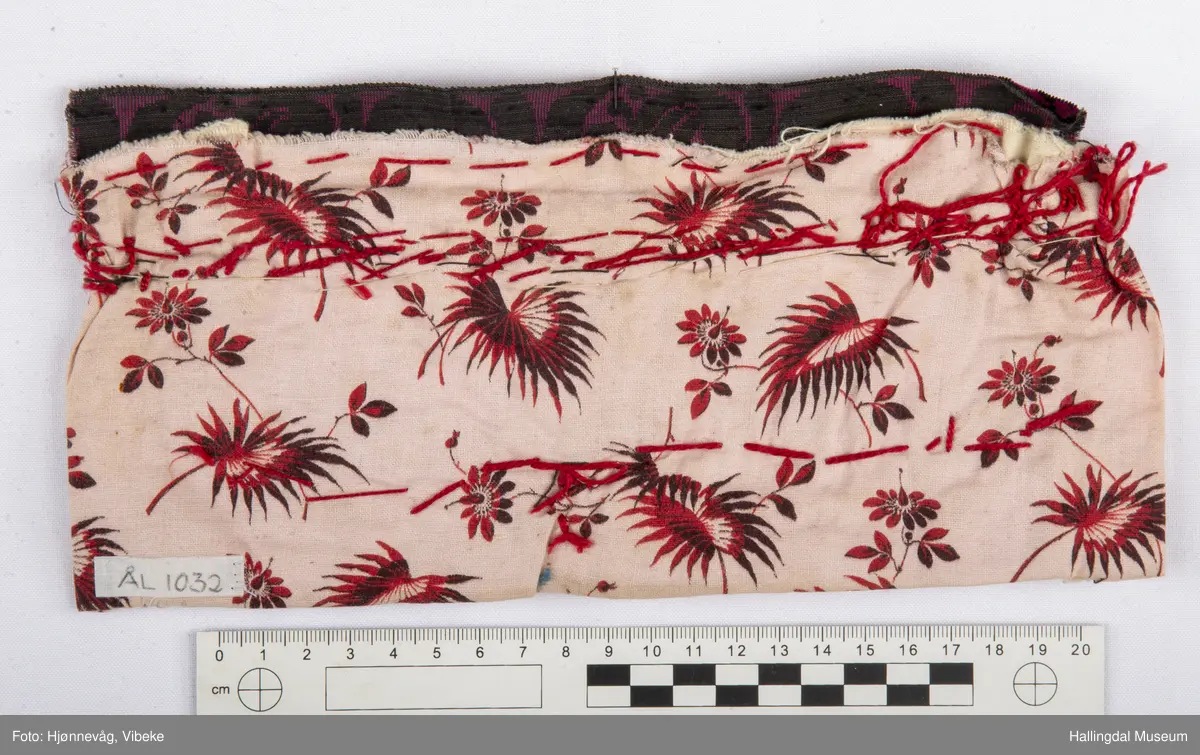 5 åttebladroser av lange glasperler, små perler rundt, over desse ei rad med store, kuleforma, blanke og lys blå perler.