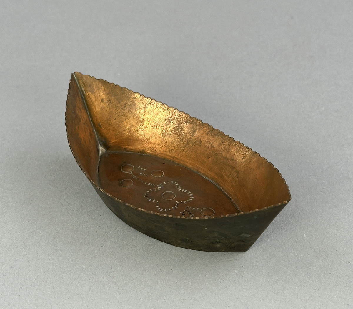 "Skål" av koppar, formad som en båt med mönster i botten.