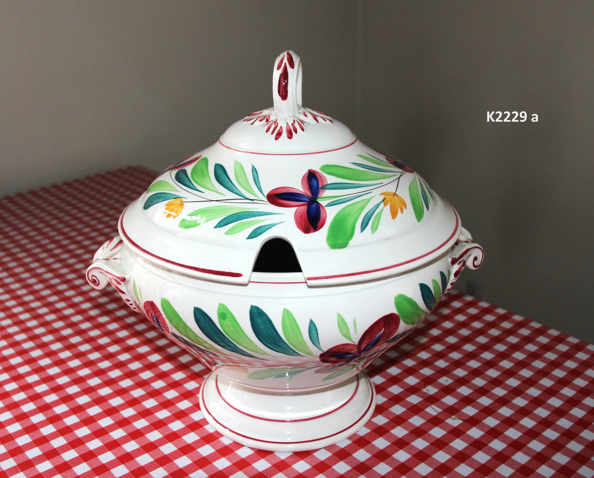 K 2229 
Servise, “Bondemønster”, Saarreguemines, 1900-åreme 
a) Terrin med lokk. 
Lokk. Hvelvet, bred bord langs kanten: grønn gren med røde og blå blomster, rund hankering med røde blad. 
b) Ovalt fat, med bord i brede strøk over bremmen. 
Stemplet i sort: Opaque de Saaregemines, H 169 A. 
c) Ovalt fat. Stemplet fabrikk merke og H 169 W. 
d) Ovalt fat. Stemplet i sort og i godset: 5 K. 
e) Båtformet skål (til pålegg). Avlang rned svakt svungne sider og konkavt buet i kortsidene. 
f) Make til e. 
g) Stettefat. 
h) Kopp. Vid rundsidet kopp, uten stett, forholdsvis lav. Stemplet i sort. 
i) Skål til koppen h).  Stemplet i sort. 
j) Kaffekanne, Pæreformet korpus, bølgende toppkontur, lang tut. Stemplet i sort og 169. Hvelvet lokk med rød toppfarge på lokkgrepet.
k) Fløtemugge, skrånende sider, riller oppe og nede , rillet hank, annerledes enn på den C-formede på kannen.
l) Sukkerkopp med lokk. Skrånende vegger, bredest nede, to hanker, riller oppe og nede, avtrappet lokk. Høyde med lokk 12,5. H. uten 7,2. Diam. bunn 10,8. 
m) Sausekopp. Eggformet skål med en skjellform i relieff , markert med rød farge, i den ene kortside, hvor hanken er. Smal liten skål med bred tut.
Fløtekopp og sukkerkopp av en annen design enn kanne, terrin og sausenebb, men samme mønster. Mønstret er det som kalles “Boerenbont” (broget bondemønster) og som ble laget først i Maastricht 
i Nederland, siden tatt opp av fabrikken Saarreguemirnes i Lorraine,og av Egersund Fayencefabrik i 1930-årene. 
n) Båtformet skål. Som e) Stemplet med sort. 
o) Ovalt fat. Stemplet Sarreguemines med sort og B 169. 
p) Terrin med lokk, stemplet med sort, og L i blindstempel.
Skrå fot, sterkt utskrånende sider, rundet av øverst, to sidehanker.
q) Underfat til terrin, rundt med to hanker. St. med sort og blindstempel: 3 R.
r) Potetfat. St. med sort og sort K.
