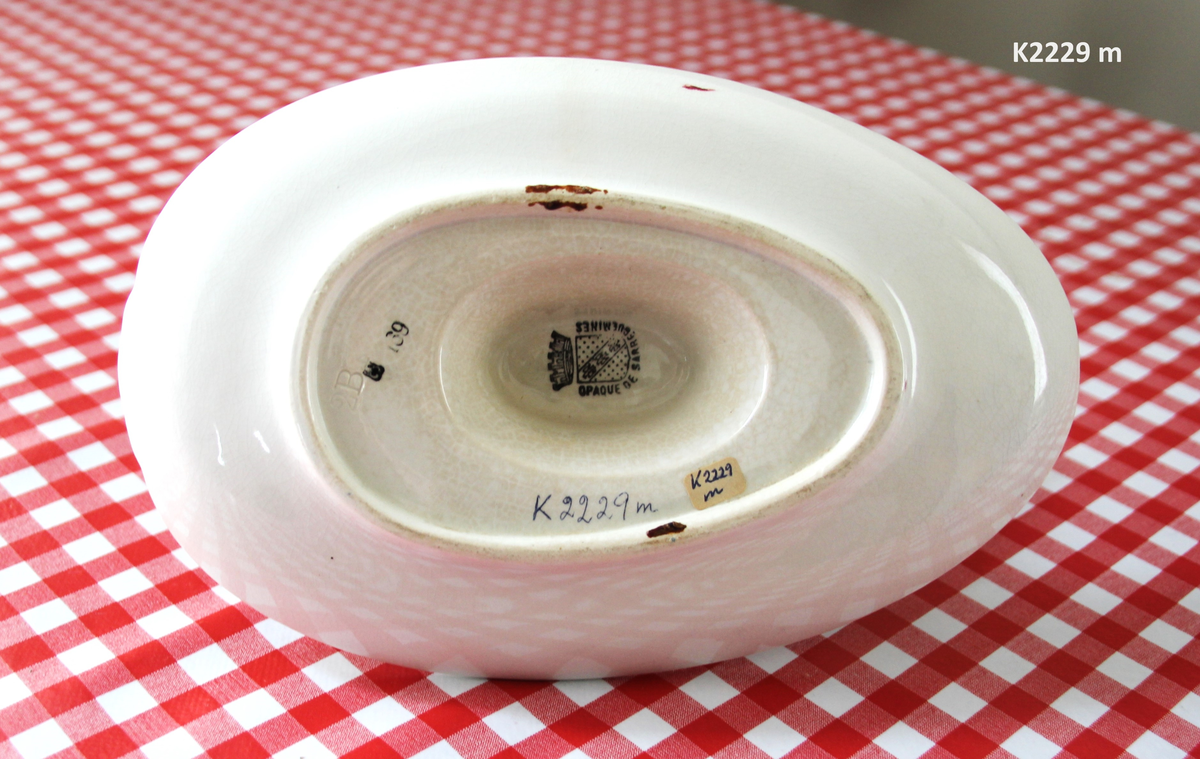 K 2229 
Servise, “Bondemønster”, Saarreguemines, 1900-åreme 
a) Terrin med lokk. 
Lokk. Hvelvet, bred bord langs kanten: grønn gren med røde og blå blomster, rund hankering med røde blad. 
b) Ovalt fat, med bord i brede strøk over bremmen. 
Stemplet i sort: Opaque de Saaregemines, H 169 A. 
c) Ovalt fat. Stemplet fabrikk merke og H 169 W. 
d) Ovalt fat. Stemplet i sort og i godset: 5 K. 
e) Båtformet skål (til pålegg). Avlang rned svakt svungne sider og konkavt buet i kortsidene. 
f) Make til e. 
g) Stettefat. 
h) Kopp. Vid rundsidet kopp, uten stett, forholdsvis lav. Stemplet i sort. 
i) Skål til koppen h).  Stemplet i sort. 
j) Kaffekanne, Pæreformet korpus, bølgende toppkontur, lang tut. Stemplet i sort og 169. Hvelvet lokk med rød toppfarge på lokkgrepet.
k) Fløtemugge, skrånende sider, riller oppe og nede , rillet hank, annerledes enn på den C-formede på kannen.
l) Sukkerkopp med lokk. Skrånende vegger, bredest nede, to hanker, riller oppe og nede, avtrappet lokk. Høyde med lokk 12,5. H. uten 7,2. Diam. bunn 10,8. 
m) Sausekopp. Eggformet skål med en skjellform i relieff , markert med rød farge, i den ene kortside, hvor hanken er. Smal liten skål med bred tut.
Fløtekopp og sukkerkopp av en annen design enn kanne, terrin og sausenebb, men samme mønster. Mønstret er det som kalles “Boerenbont” (broget bondemønster) og som ble laget først i Maastricht 
i Nederland, siden tatt opp av fabrikken Saarreguemirnes i Lorraine,og av Egersund Fayencefabrik i 1930-årene. 
n) Båtformet skål. Som e) Stemplet med sort. 
o) Ovalt fat. Stemplet Sarreguemines med sort og B 169. 
p) Terrin med lokk, stemplet med sort, og L i blindstempel.
Skrå fot, sterkt utskrånende sider, rundet av øverst, to sidehanker.
q) Underfat til terrin, rundt med to hanker. St. med sort og blindstempel: 3 R.
r) Potetfat. St. med sort og sort K.