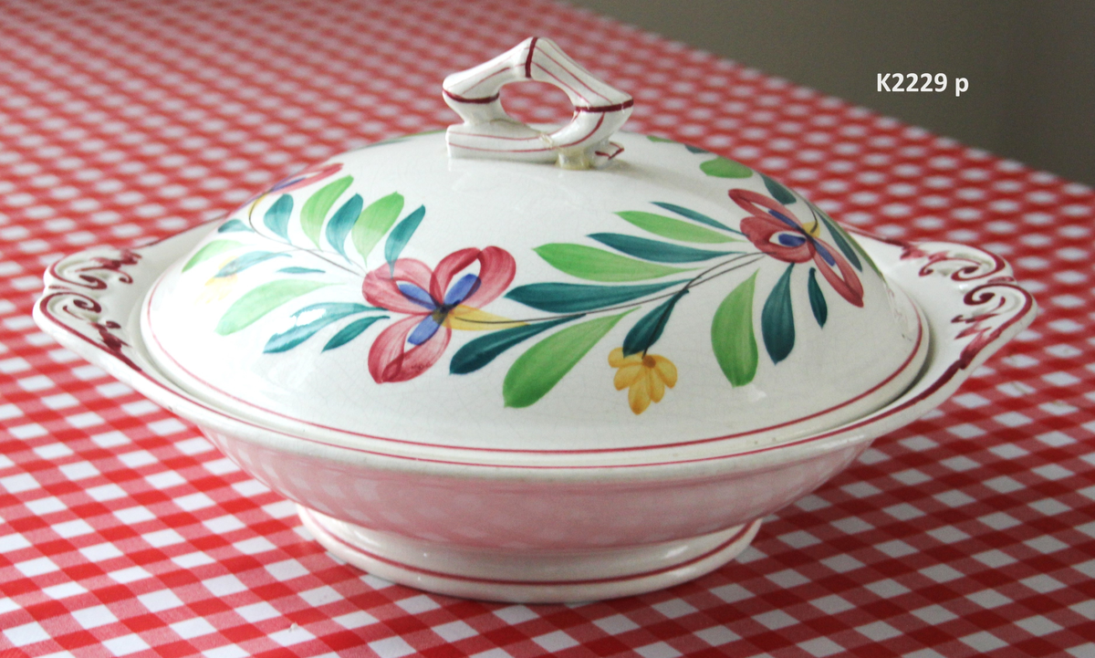 K 2229 
Servise, “Bondemønster”, Saarreguemines, 1900-åreme 
a) Terrin med lokk. 
Lokk. Hvelvet, bred bord langs kanten: grønn gren med røde og blå blomster, rund hankering med røde blad. 
b) Ovalt fat, med bord i brede strøk over bremmen. 
Stemplet i sort: Opaque de Saaregemines, H 169 A. 
c) Ovalt fat. Stemplet fabrikk merke og H 169 W. 
d) Ovalt fat. Stemplet i sort og i godset: 5 K. 
e) Båtformet skål (til pålegg). Avlang rned svakt svungne sider og konkavt buet i kortsidene. 
f) Make til e. 
g) Stettefat. 
h) Kopp. Vid rundsidet kopp, uten stett, forholdsvis lav. Stemplet i sort. 
i) Skål til koppen h).  Stemplet i sort. 
j) Kaffekanne, Pæreformet korpus, bølgende toppkontur, lang tut. Stemplet i sort og 169. Hvelvet lokk med rød toppfarge på lokkgrepet.
k) Fløtemugge, skrånende sider, riller oppe og nede , rillet hank, annerledes enn på den C-formede på kannen.
l) Sukkerkopp med lokk. Skrånende vegger, bredest nede, to hanker, riller oppe og nede, avtrappet lokk. Høyde med lokk 12,5. H. uten 7,2. Diam. bunn 10,8. 
m) Sausekopp. Eggformet skål med en skjellform i relieff , markert med rød farge, i den ene kortside, hvor hanken er. Smal liten skål med bred tut.
Fløtekopp og sukkerkopp av en annen design enn kanne, terrin og sausenebb, men samme mønster. Mønstret er det som kalles “Boerenbont” (broget bondemønster) og som ble laget først i Maastricht 
i Nederland, siden tatt opp av fabrikken Saarreguemirnes i Lorraine,og av Egersund Fayencefabrik i 1930-årene. 
n) Båtformet skål. Som e) Stemplet med sort. 
o) Ovalt fat. Stemplet Sarreguemines med sort og B 169. 
p) Terrin med lokk, stemplet med sort, og L i blindstempel.
Skrå fot, sterkt utskrånende sider, rundet av øverst, to sidehanker.
q) Underfat til terrin, rundt med to hanker. St. med sort og blindstempel: 3 R.
r) Potetfat. St. med sort og sort K.