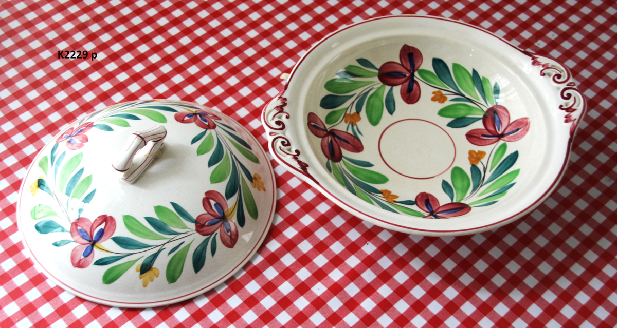 K 2229 
Servise, “Bondemønster”, Saarreguemines, 1900-åreme 
a) Terrin med lokk. 
Lokk. Hvelvet, bred bord langs kanten: grønn gren med røde og blå blomster, rund hankering med røde blad. 
b) Ovalt fat, med bord i brede strøk over bremmen. 
Stemplet i sort: Opaque de Saaregemines, H 169 A. 
c) Ovalt fat. Stemplet fabrikk merke og H 169 W. 
d) Ovalt fat. Stemplet i sort og i godset: 5 K. 
e) Båtformet skål (til pålegg). Avlang rned svakt svungne sider og konkavt buet i kortsidene. 
f) Make til e. 
g) Stettefat. 
h) Kopp. Vid rundsidet kopp, uten stett, forholdsvis lav. Stemplet i sort. 
i) Skål til koppen h).  Stemplet i sort. 
j) Kaffekanne, Pæreformet korpus, bølgende toppkontur, lang tut. Stemplet i sort og 169. Hvelvet lokk med rød toppfarge på lokkgrepet.
k) Fløtemugge, skrånende sider, riller oppe og nede , rillet hank, annerledes enn på den C-formede på kannen.
l) Sukkerkopp med lokk. Skrånende vegger, bredest nede, to hanker, riller oppe og nede, avtrappet lokk. Høyde med lokk 12,5. H. uten 7,2. Diam. bunn 10,8. 
m) Sausekopp. Eggformet skål med en skjellform i relieff , markert med rød farge, i den ene kortside, hvor hanken er. Smal liten skål med bred tut.
Fløtekopp og sukkerkopp av en annen design enn kanne, terrin og sausenebb, men samme mønster. Mønstret er det som kalles “Boerenbont” (broget bondemønster) og som ble laget først i Maastricht 
i Nederland, siden tatt opp av fabrikken Saarreguemirnes i Lorraine,og av Egersund Fayencefabrik i 1930-årene. 
n) Båtformet skål. Som e) Stemplet med sort. 
o) Ovalt fat. Stemplet Sarreguemines med sort og B 169. 
p) Terrin med lokk, stemplet med sort, og L i blindstempel.
Skrå fot, sterkt utskrånende sider, rundet av øverst, to sidehanker.
q) Underfat til terrin, rundt med to hanker. St. med sort og blindstempel: 3 R.
r) Potetfat. St. med sort og sort K.