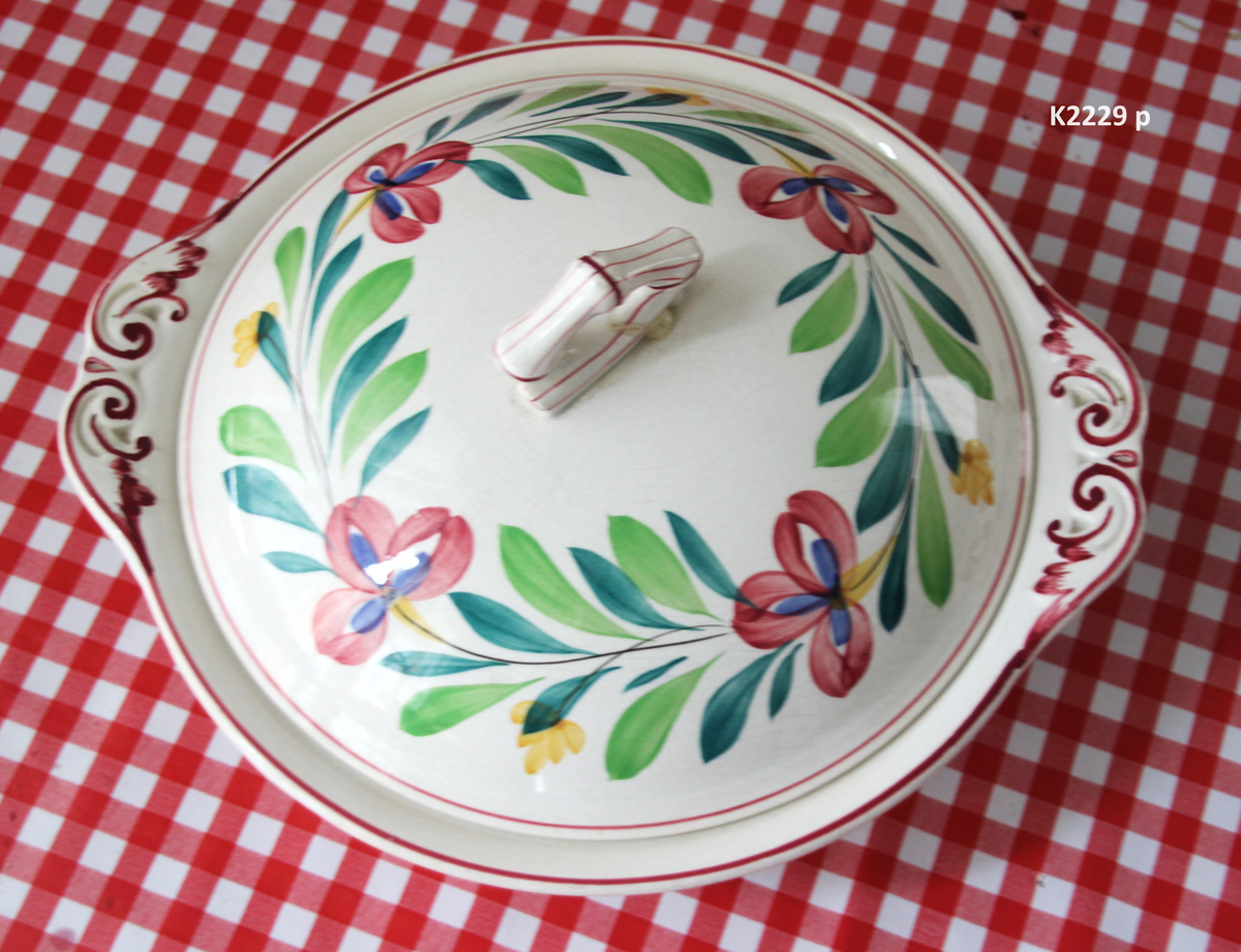 K 2229 
Servise, “Bondemønster”, Saarreguemines, 1900-åreme 
a) Terrin med lokk. 
Lokk. Hvelvet, bred bord langs kanten: grønn gren med røde og blå blomster, rund hankering med røde blad. 
b) Ovalt fat, med bord i brede strøk over bremmen. 
Stemplet i sort: Opaque de Saaregemines, H 169 A. 
c) Ovalt fat. Stemplet fabrikk merke og H 169 W. 
d) Ovalt fat. Stemplet i sort og i godset: 5 K. 
e) Båtformet skål (til pålegg). Avlang rned svakt svungne sider og konkavt buet i kortsidene. 
f) Make til e. 
g) Stettefat. 
h) Kopp. Vid rundsidet kopp, uten stett, forholdsvis lav. Stemplet i sort. 
i) Skål til koppen h).  Stemplet i sort. 
j) Kaffekanne, Pæreformet korpus, bølgende toppkontur, lang tut. Stemplet i sort og 169. Hvelvet lokk med rød toppfarge på lokkgrepet.
k) Fløtemugge, skrånende sider, riller oppe og nede , rillet hank, annerledes enn på den C-formede på kannen.
l) Sukkerkopp med lokk. Skrånende vegger, bredest nede, to hanker, riller oppe og nede, avtrappet lokk. Høyde med lokk 12,5. H. uten 7,2. Diam. bunn 10,8. 
m) Sausekopp. Eggformet skål med en skjellform i relieff , markert med rød farge, i den ene kortside, hvor hanken er. Smal liten skål med bred tut.
Fløtekopp og sukkerkopp av en annen design enn kanne, terrin og sausenebb, men samme mønster. Mønstret er det som kalles “Boerenbont” (broget bondemønster) og som ble laget først i Maastricht 
i Nederland, siden tatt opp av fabrikken Saarreguemirnes i Lorraine,og av Egersund Fayencefabrik i 1930-årene. 
n) Båtformet skål. Som e) Stemplet med sort. 
o) Ovalt fat. Stemplet Sarreguemines med sort og B 169. 
p) Terrin med lokk, stemplet med sort, og L i blindstempel.
Skrå fot, sterkt utskrånende sider, rundet av øverst, to sidehanker.
q) Underfat til terrin, rundt med to hanker. St. med sort og blindstempel: 3 R.
r) Potetfat. St. med sort og sort K.