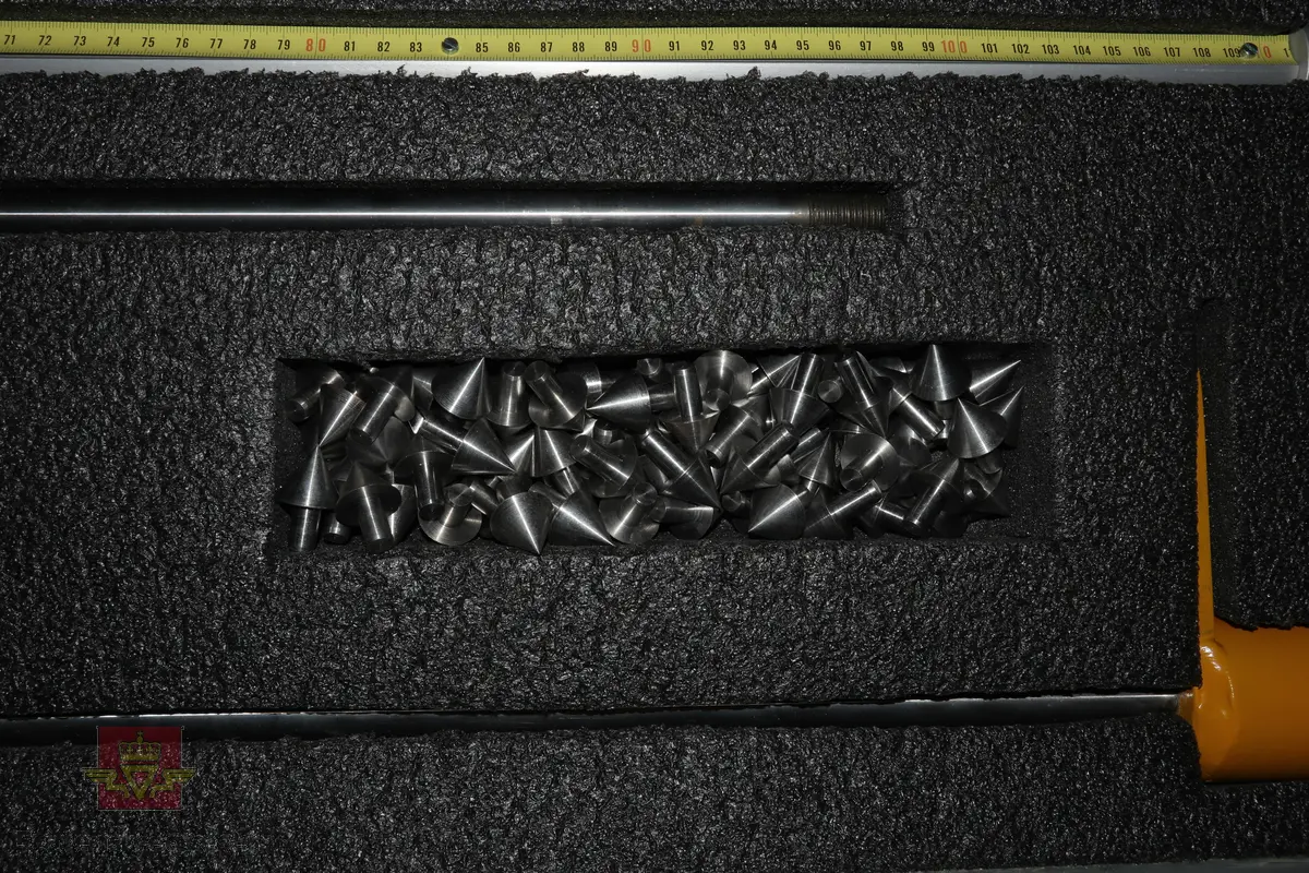 Sort trekasse med bærehåndtak som inneholder et mekanisk målemeter av stål som består av flere bevegelige deler som en sleidehammer med måleskala. I bunnen av utstyret sitter en utskiftbar metallspiss. Kofferten inneholder 40stk ekstra metallspisser.