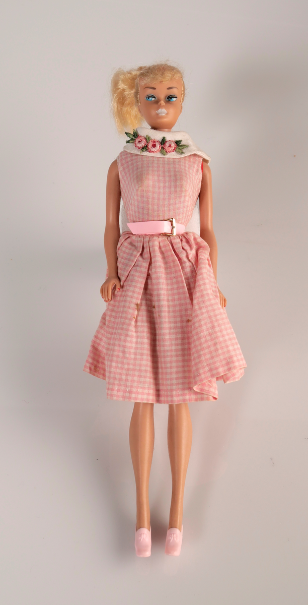 Barbiedocka med ljust hår. Rosarutig klänning med broderade blommor på vit krage. Rosa skärp och rosa klackskor. Till dockan har givaren och hennes mamma gjort egna kläder.

1a: Barbiedocka
1b: Klänning
1c: Skärp
1d-e: Skor

Dräktdelar till barbie. Hemgjorda av givaren eller hennes mamma. 
2ab: Orange dräkt bestående av tröja och kjol. 
3a-d: Virkad gul dräkt bestående av jacka, kjol, väska och hatt.
4: Virkad röd jacka. 
5: Virkad rosa jacka. 
6: Bruna manchesterbyxor. 
7: Blå halsduk
8: Beige hatt 
9: Röd tröja med vit kant. 
10: Röd mössa/halsduk
11: Blågul mössa 
12: Vit brudklänning
13: Blå klänning med vit spets.