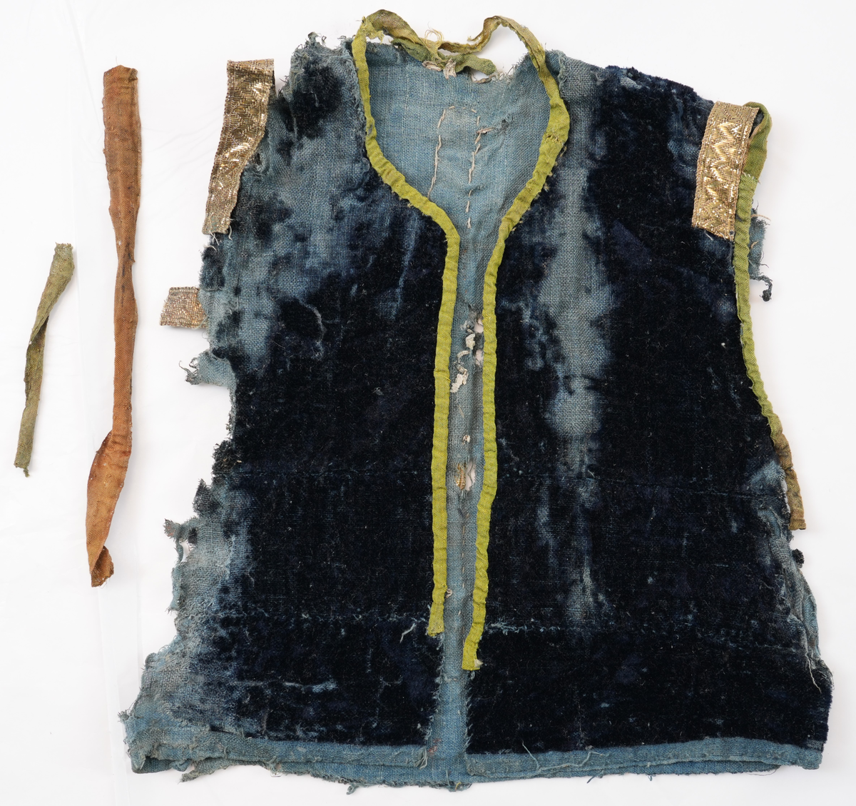 Opplut i blå plysj med blått linfôr. Rund halsringing og litt skrådd opning framme. Ikkje skuldersaum, men eit insnitt på skuldra mot ermopningen. Framkant og hals er kvarda med eit gulgrønt lerretsvove silkeband, og ermopning er kvarda med grønt silkeband med lys jarekant. Ermopning på bakstykke og eit stykke ned på framstykke er prydd med gylte sølvborder. Ryggen har ei bord midt på  og i to motståande vinklar på kvar side av midtborda.
Lause trådar i ermopningen tyder på at det har vore ermer i oppluten.
Det er 2 skøyter på framstykket ein 23 cm ned frå skulder og ein 39 cm ned.