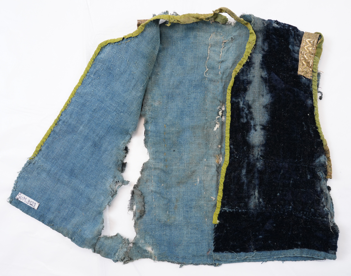 Opplut i blå plysj med blått linfôr. Rund halsringing og litt skrådd opning framme. Ikkje skuldersaum, men eit insnitt på skuldra mot ermopningen. Framkant og hals er kvarda med eit gulgrønt lerretsvove silkeband, og ermopning er kvarda med grønt silkeband med lys jarekant. Ermopning på bakstykke og eit stykke ned på framstykke er prydd med gylte sølvborder. Ryggen har ei bord midt på  og i to motståande vinklar på kvar side av midtborda.
Lause trådar i ermopningen tyder på at det har vore ermer i oppluten.
Det er 2 skøyter på framstykket ein 23 cm ned frå skulder og ein 39 cm ned.