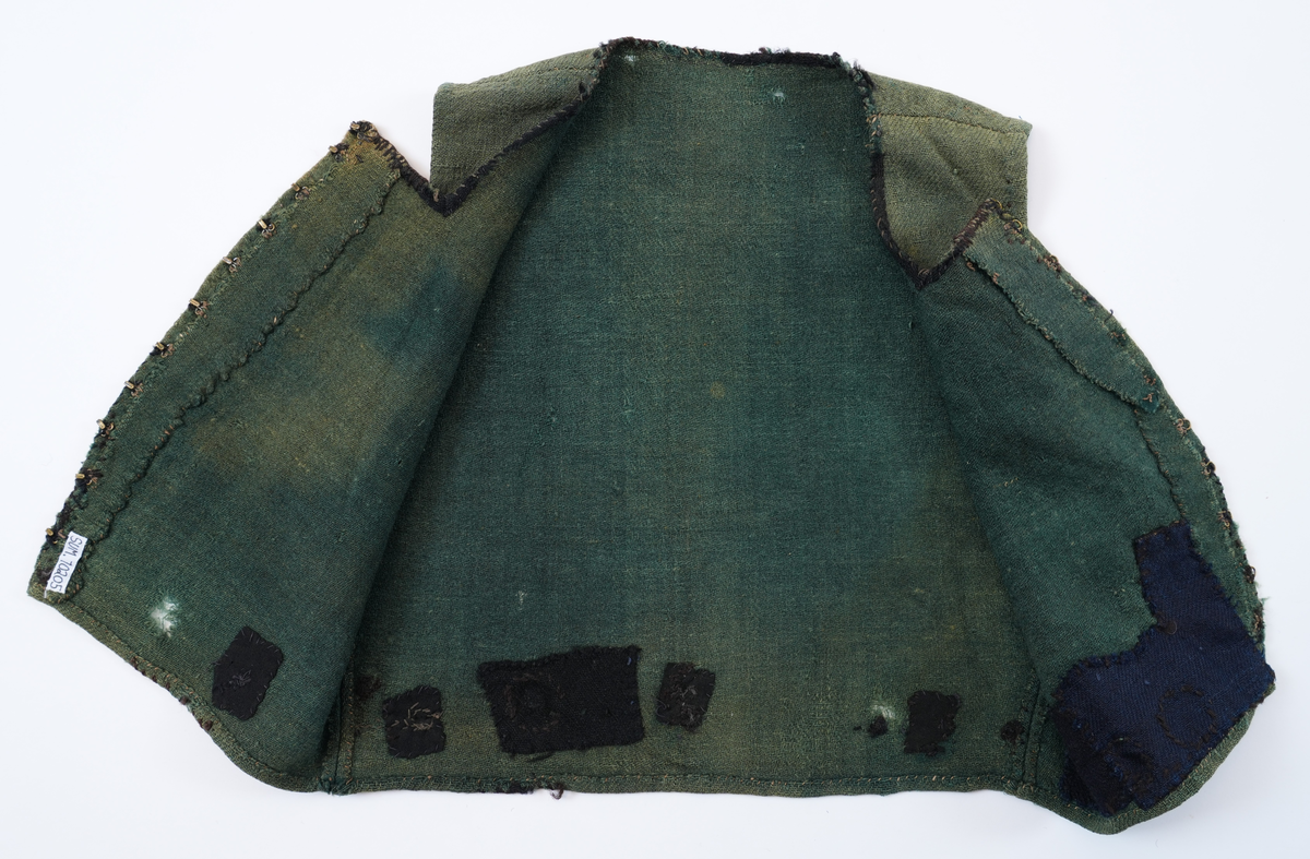 Livstykke som er overdel til kvinnedrakt. Livstykke i grønn ull med firskoren halsopning. Skal festast heilt ihop framme med 11 sett hekter og hemper. Hekter og hemper rundt livet til feste for skjørt. Rundt ermeopningane har det vore enkel fald, seinare er dette stadvis forsterka med overkast av grov tråd. Det same er tilfellet rundt halsopningen der det opphavleg har vore svart ullband. Livstykket er reparert med svarte og blå bøter i nedkant. Framkanten på livet er runda for å lage plass til bysten.