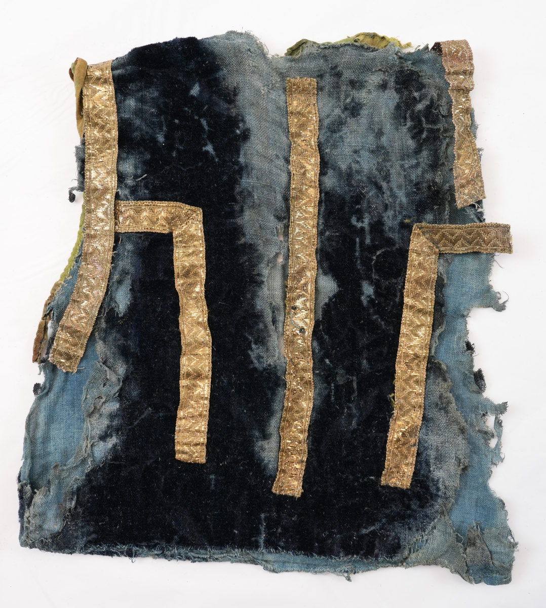 Opplut i blå plysj med blått linfôr. Rund halsringing og litt skrådd opning framme. Ikkje skuldersaum, men eit insnitt på skuldra mot ermopningen. Framkant og hals er kvarda med eit gulgrønt lerretsvove silkeband, og ermopning er kvarda med grønt silkeband med lys jarekant. Ermopning på bakstykke og eit stykke ned på framstykke er prydd med gylte sølvborder. Ryggen har ei bord midt på  og i to motståande vinklar på kvar side av midtborda.
Lause trådar i ermopningen tyder på at det har vore ermer i oppluten.
Det er 2 skøyter på framstykket ein 23 cm ned frå skulder og ein 39 cm ned.